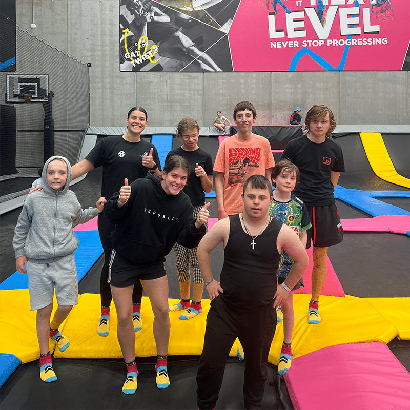 A group of young people standing together smiling on trampolines at an activity centre